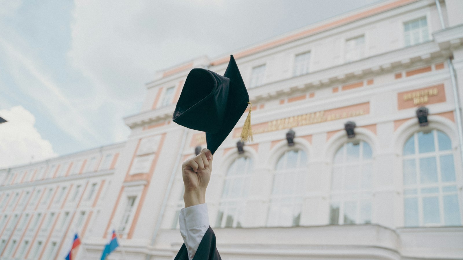 Graduate holding a graduation cap in front of a university building