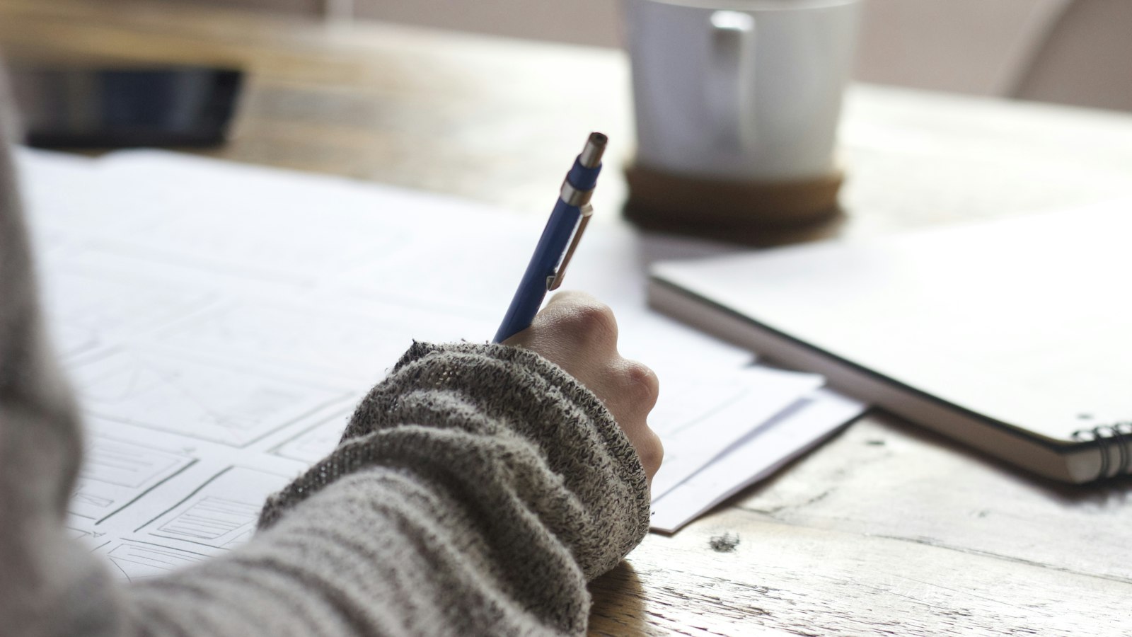 Student writing notes at a wooden table while preparing for a final exam